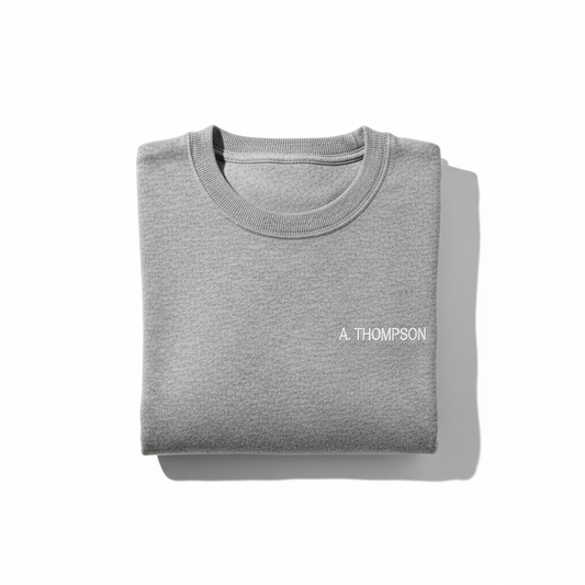 Grey crew neck sweater with embroidered name on left chest, flat lay on white background